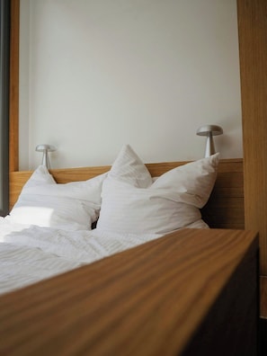 Ein ordentlich bezogenes Bett mit weißen Leinen und Kissen, ein Holzkopfende und zwei Nachttischlampen.