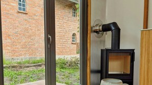 A room with a large window, a book on a small table, a white mug, and a black wood-burning stove. - Modern tiny house with private lake access (Walsrode)