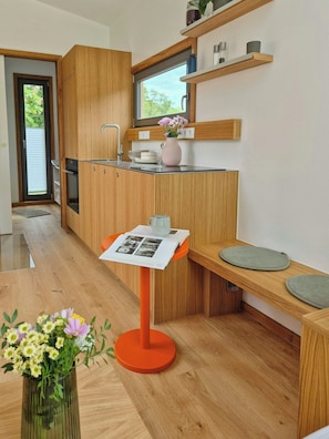 Eine moderne Küche mit Holzausstattung, integriertem Backofen, einem Fenster und einem kleinen Tisch mit Blumen in einer Vase.