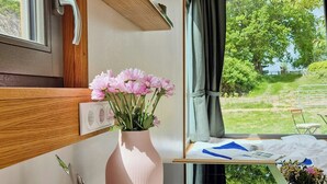 A kitchen area with a window view, a pink vase with flowers, and a dining set. - Modern tiny house with private lake access (Walsrode)