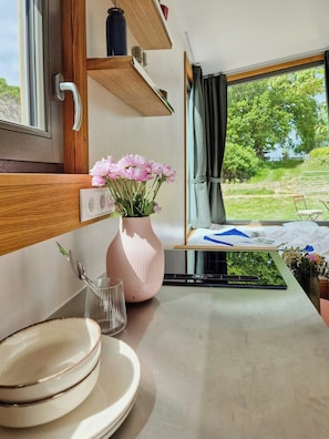 Ein Küchenbereich mit Fensterblick, eine rosafarbene Vase mit Blumen und ein Esstisch mit Stühlen.