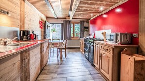 Eine Holz-Küche mit roter Akzentwand, ein Essbereich mit Tisch und Stühlen sowie ein Blick ins Freie durch ein Fenster.