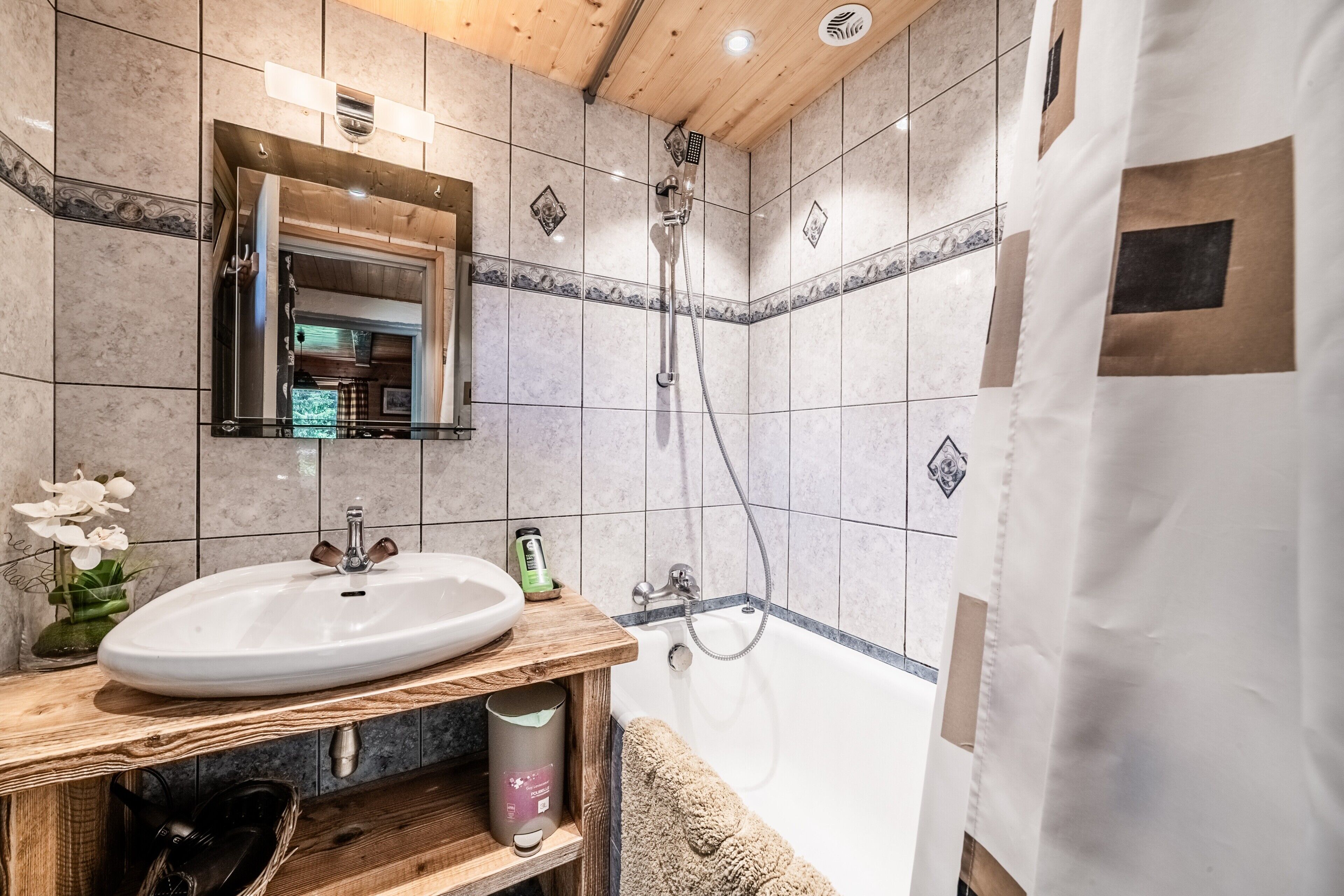 Ein Badezimmer mit einem Holzbadschränkchen, einem Waschbecken, einem Spiegel, einer Dusche und einer Badewanne.