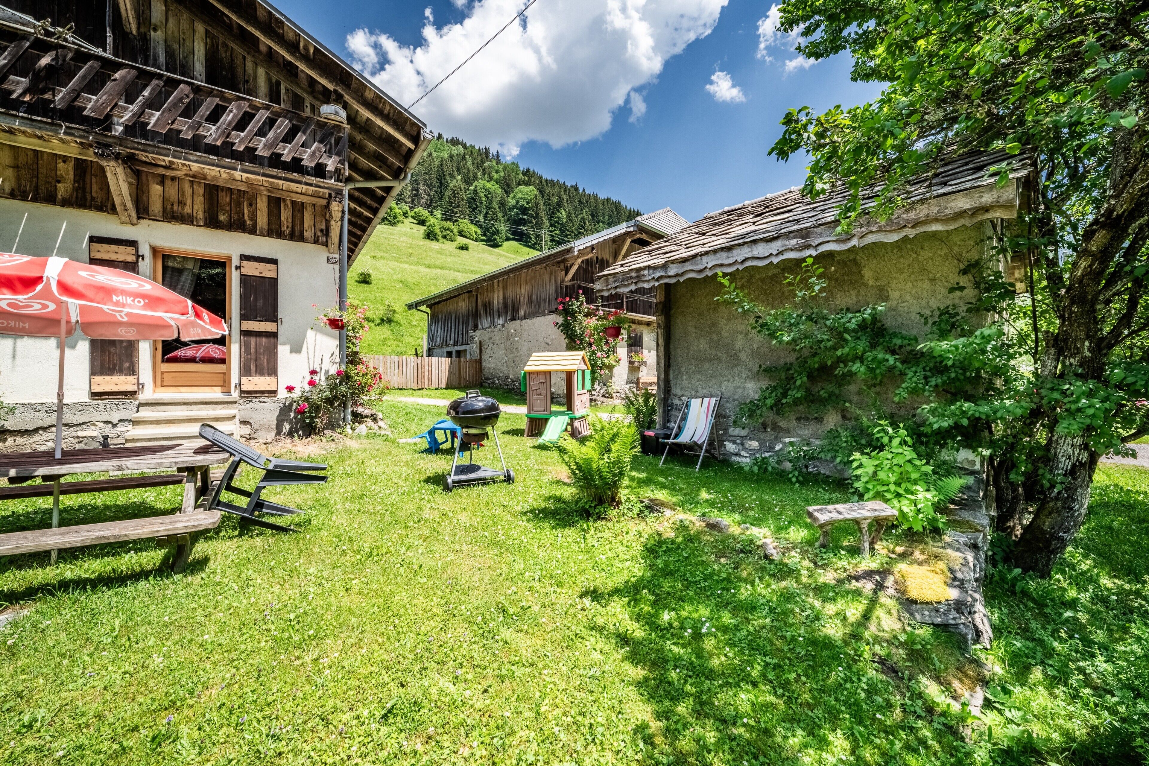 Un bâtiment de style rustique, avec une façade en bois, un petit jardin agrémenté d’une table de pique-nique et d’un barbecue.