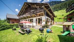 Ein rustikales Holzhaus mit Balkon, Grill und einem Spielhäuschen für Kinder.
