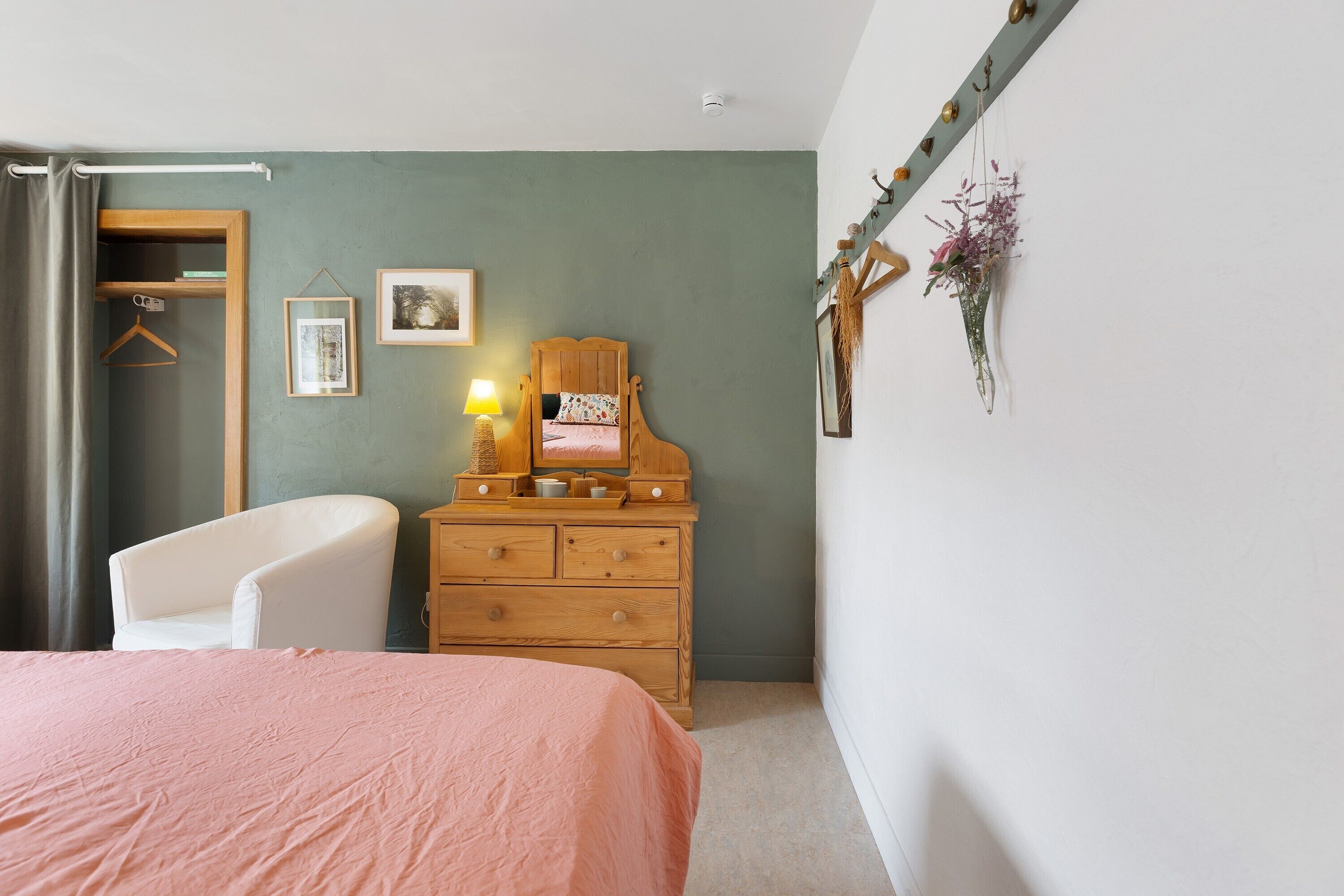 Un dormitorio con cama, cómoda, silla, perchero y una pared con un cuadro y una lámpara.