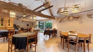 A restaurant with wooden tables and chairs, hanging baskets, and a view of greenery outside.