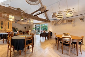 A restaurant with wooden tables and chairs, hanging baskets, and a view of greenery outside.