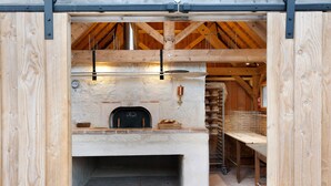 A rustic stone fireplace with a bread basket and a pizza oven, wooden beams, and a brick floor.