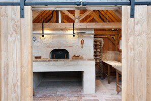 A rustic wooden interior with a brick floor, a stone fireplace, and a bread oven.