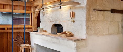 A rustic kitchen with a stone oven, wooden beams, and a hanging light fixture.