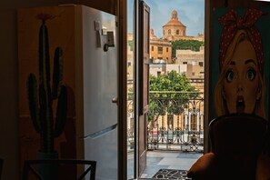 Eine offene Tür, die auf einen Balkon mit Blick auf ein Gebäude mit Kuppeln und einer Kaktusdekoration führt.
