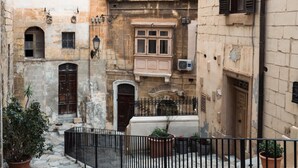 Un carrer estret amb edificis antics, una tanca de metall negre i plantes en testos.