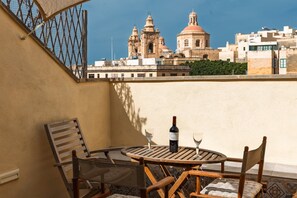 Ein Balkon mit Tisch, Stühlen, einer Weinflasche und Gläsern, mit Blick auf ein historisches Gebäude mit Kuppeln.