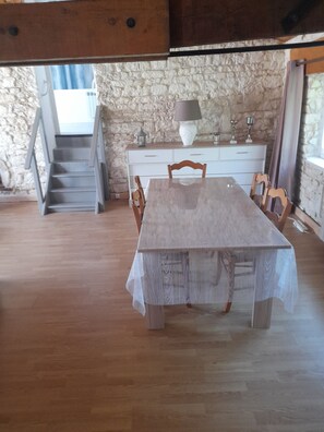Un espace repas comprenant une table en bois, des chaises, un escalier et un mur en pierre.