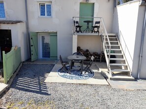 Une cour avec une table et des chaises, une porte verte, un escalier et une pile de bûches.