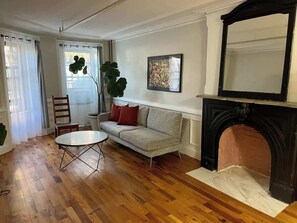 Ein Wohnzimmer mit Holzboden, einer Couch, einem Couchtisch, einem Kamin und einem großen Fenster mit Vorhängen.