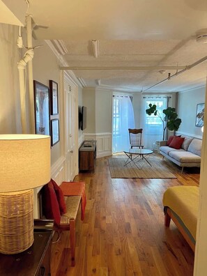 Ein Wohnzimmer mit Sofa, Sessel, Lampe, Fernseher und einer Pflanze.