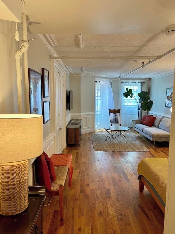 A living room with a sofa, a chair, a lamp, a television, and a plant.