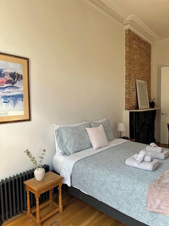 A bedroom with a bed, bedside table, radiator, and a painting on the wall.. Brooklyn stylish studio apartment!