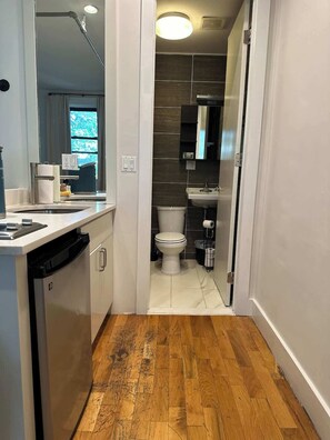 Ein schmales Gang, der zu einem Badezimmer mit Toilette, Waschbecken und Spiegel führt.
