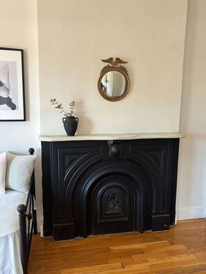 Ein schwarzer Kamin mit dekorativem Spiegel darüber, eine Vase mit Pflanzen und ein gerahmtes Bild an der Wand.
