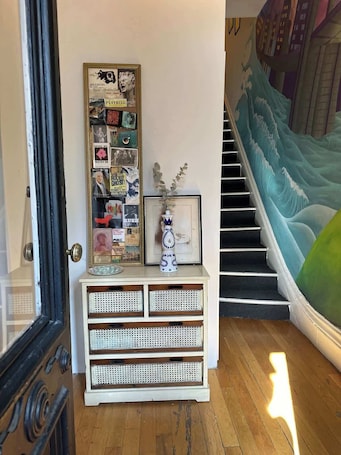 A staircase with a wave mural, a white console table with decorative items, and a door with a glass panel.. Brooklyn artistic studio apartment!