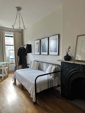 Une chambre à coucher comprenant un lit, une table, une chaise, une cheminée et trois tableaux encadrés accrochés au mur.