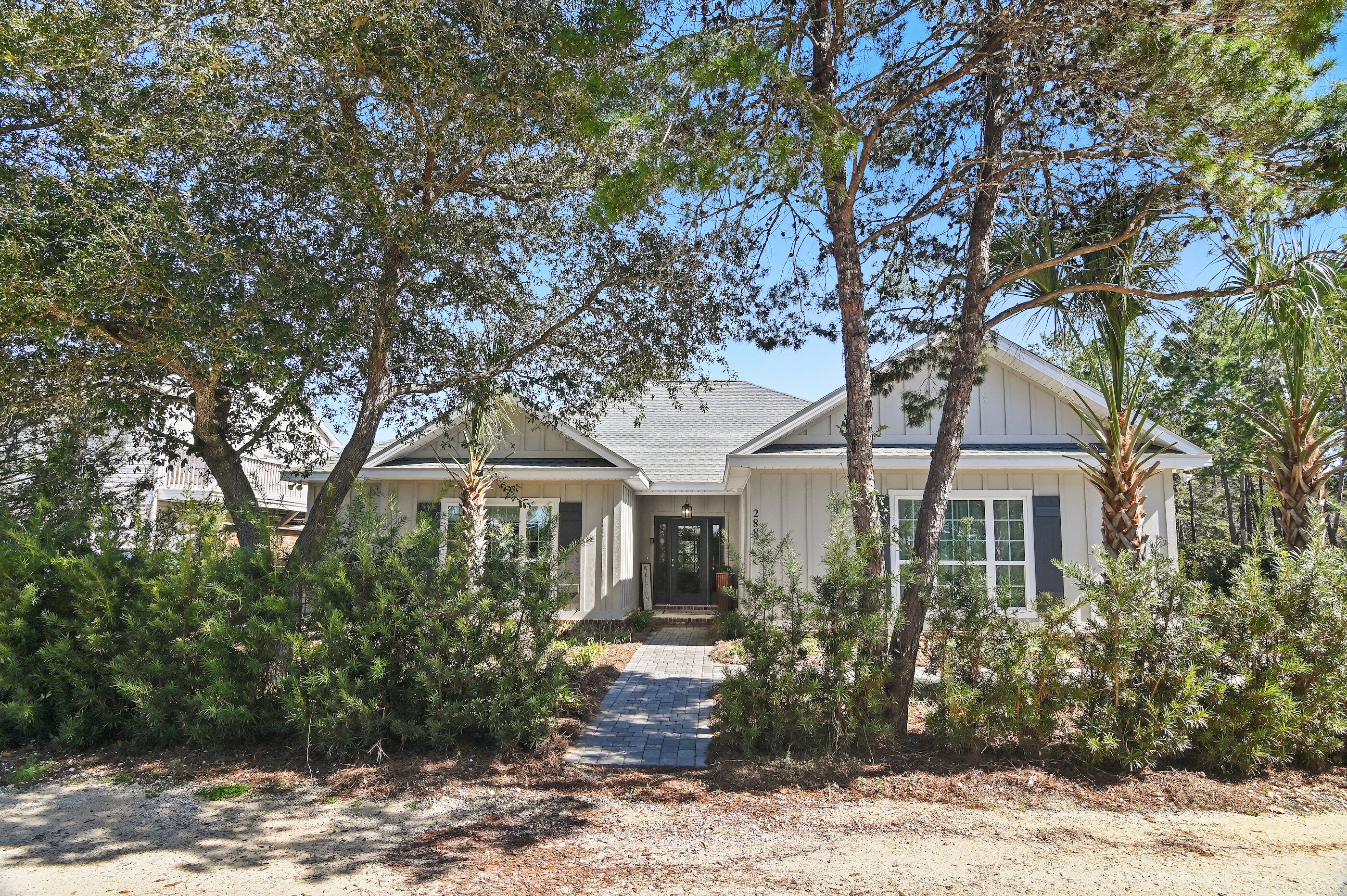 A single-story house with a front porch, surrounded by trees and a gravel driveway.