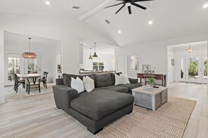 A spacious living area with a grey sectional sofa, a dining table with chairs, and a kitchen in the background. - 🌊Walk to Beach | 6 Bikes | 30A | Abbys Abode🌊 (Santa Rosa Beach)