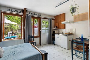 Une cuisine compacte avec un coin repas, un lit et une vue sur l’extérieur, visible à travers une porte.