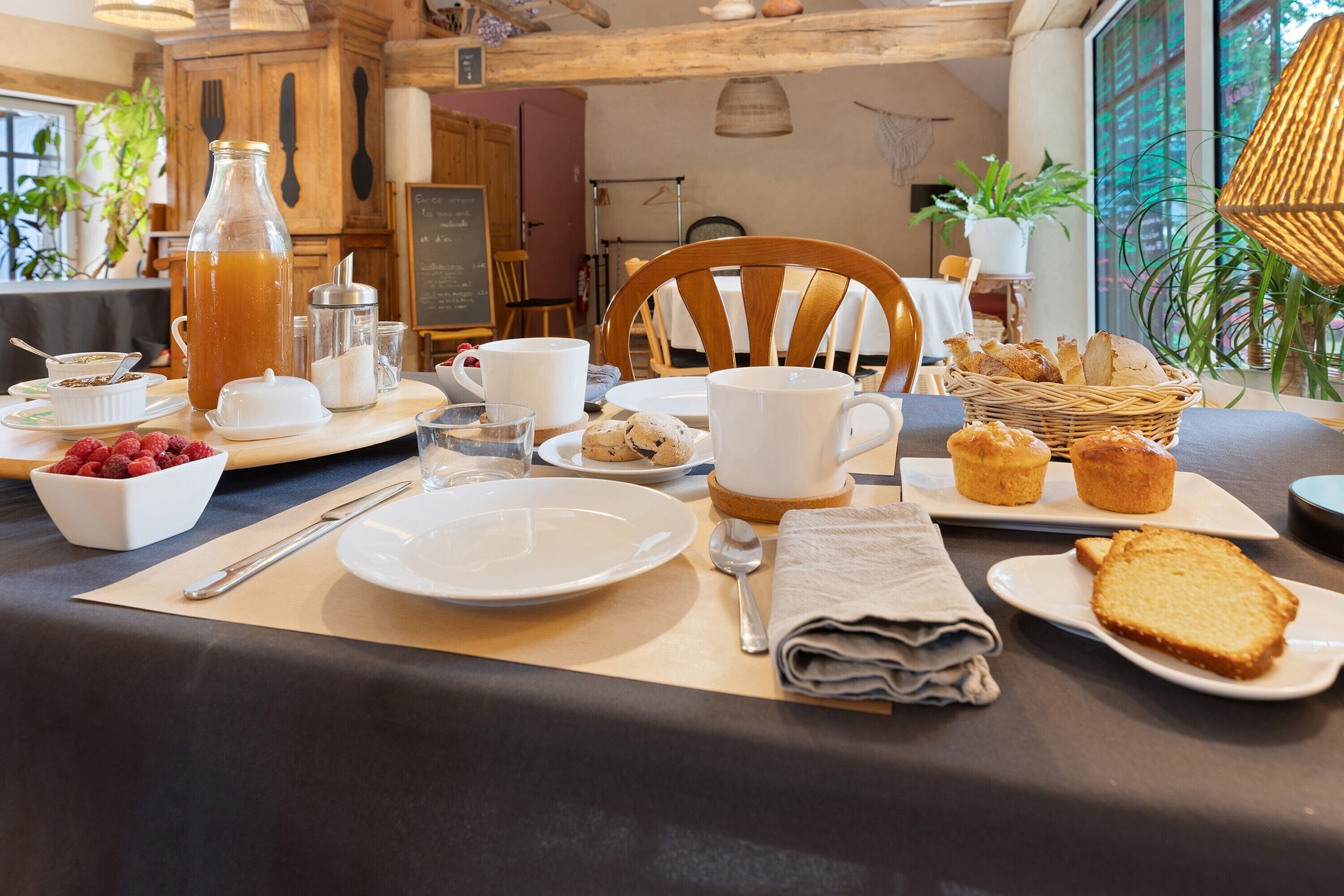 A breakfast table set with various dishes, a pitcher of juice, and a wicker basket with bread.