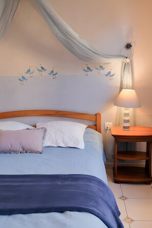 Ein Schlafzimmer mit einem Bett, Kissen, einem Nachttisch mit Lampe, einer Wand mit Vogelmotiven und einem Vorhang.