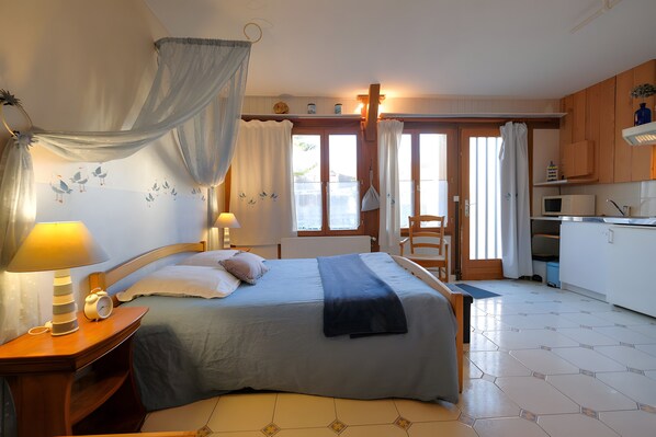 Ein Schlafzimmer mit Bett, Nachttischlampen, einem Nachttisch, einem Fenster mit Vorhängen und Blick ins Freie.