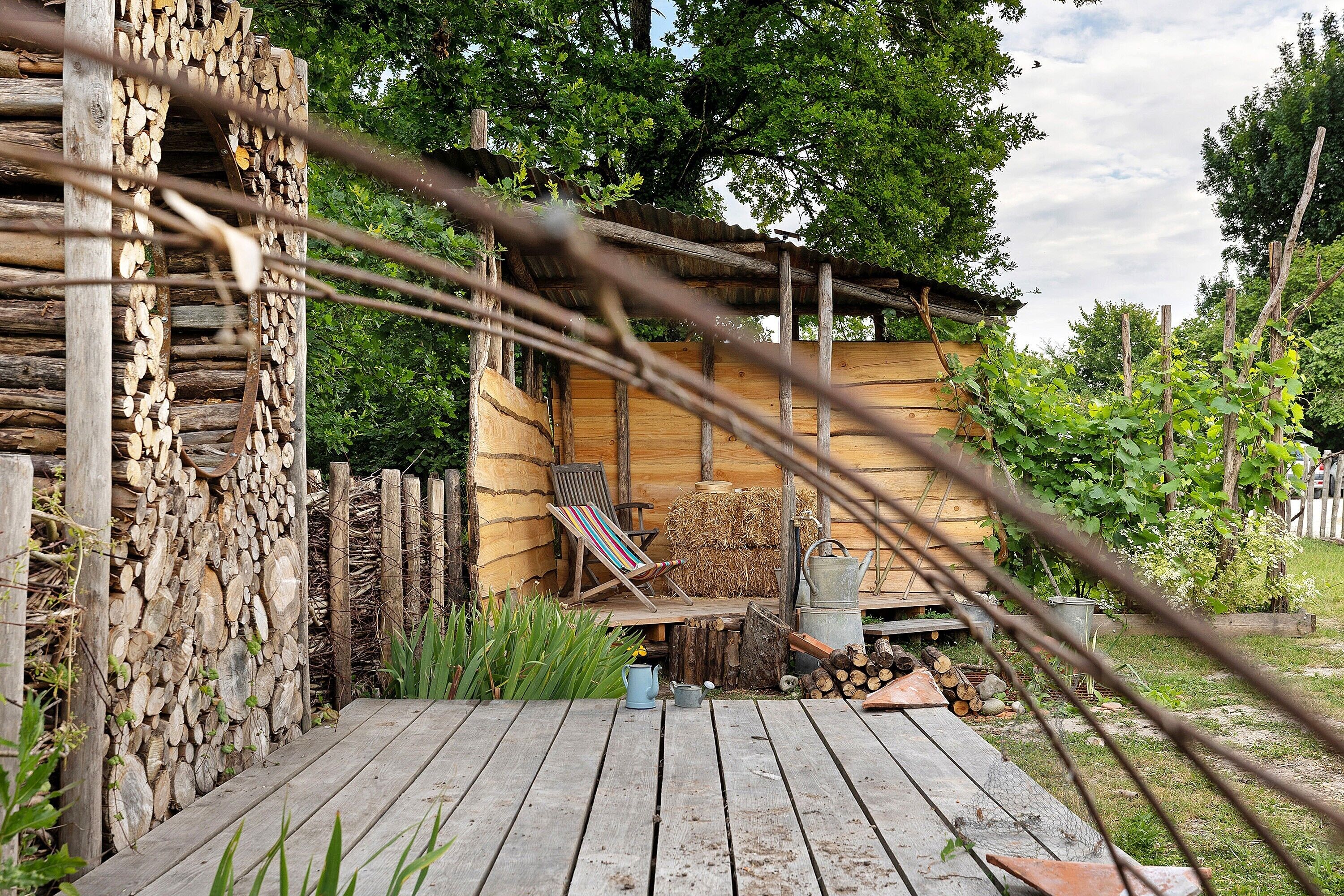 Une cabane en bois rustique avec une terrasse en bois, une chaise et un petit coin jardin.
