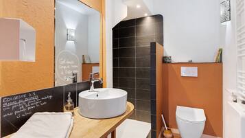 Un baño con lavamanos blanco, espejo, pared de azulejos negros y retrete blanco.