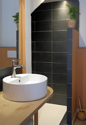 Une salle de bain avec un lavabo blanc, des carreaux noirs et un plan de travail en bois.