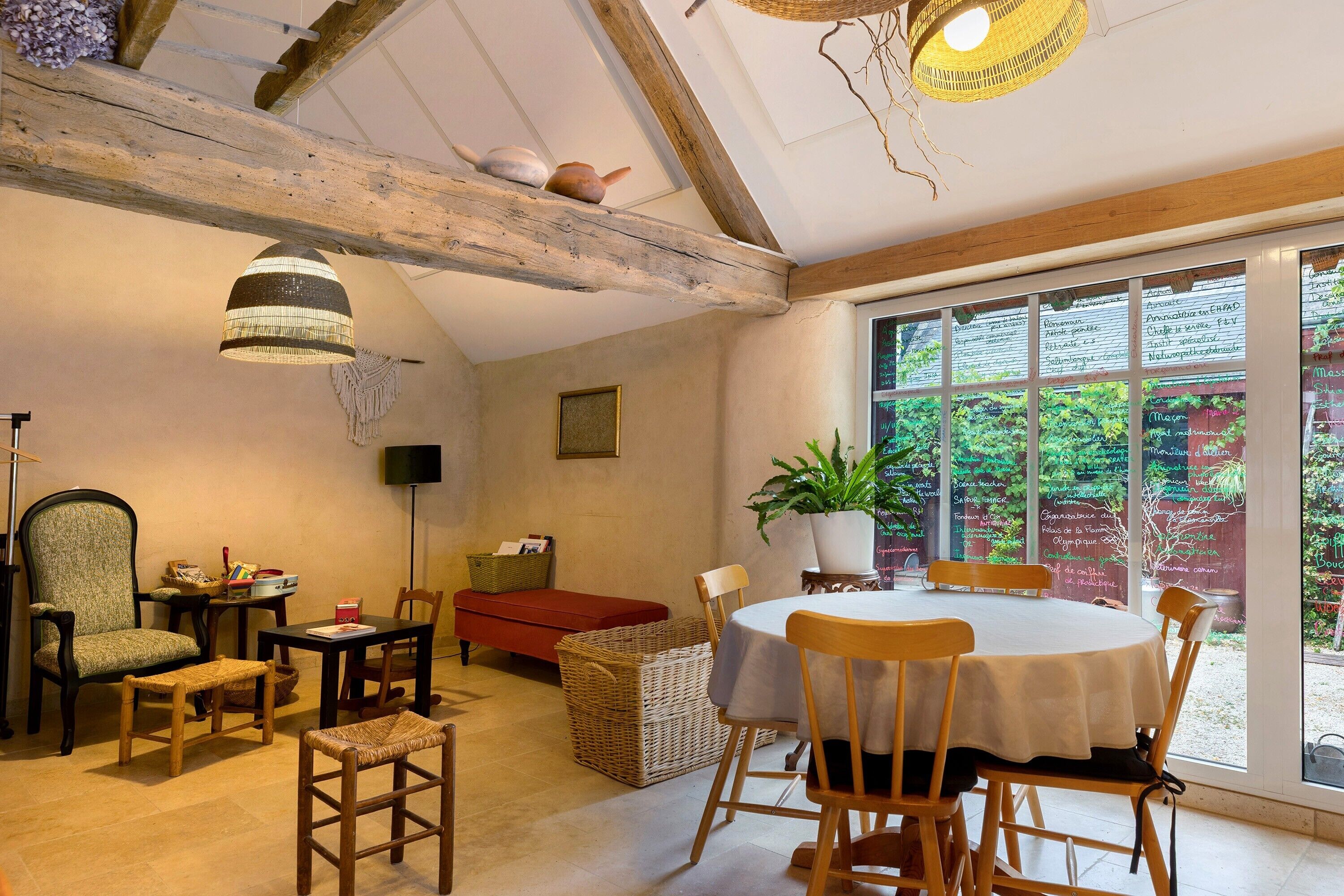 A dining area with a round table, chairs, a red bench, wicker baskets, and a potted plant.