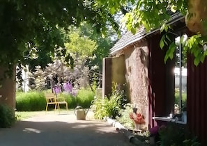 Un bâtiment rustique, doté d’un toit en pente, entouré d’une végétation luxuriante et de plantes en fleurs.