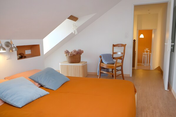 Een slaapkamer met een bed, kussens, een stoel, een klein tafeltje en een mand.