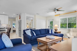 A modern living room with a sectional sofa, a coffee table, and a dining area with a kitchen in the background. - Duck Key Waterfront Paradise B Private Balcony (Duck Key)