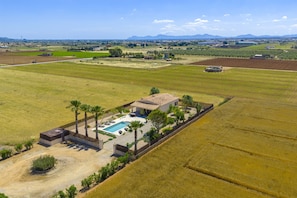Ein weitläufiges Anwesen mit Swimmingpool, Palmen und ausgedehnten Feldern.