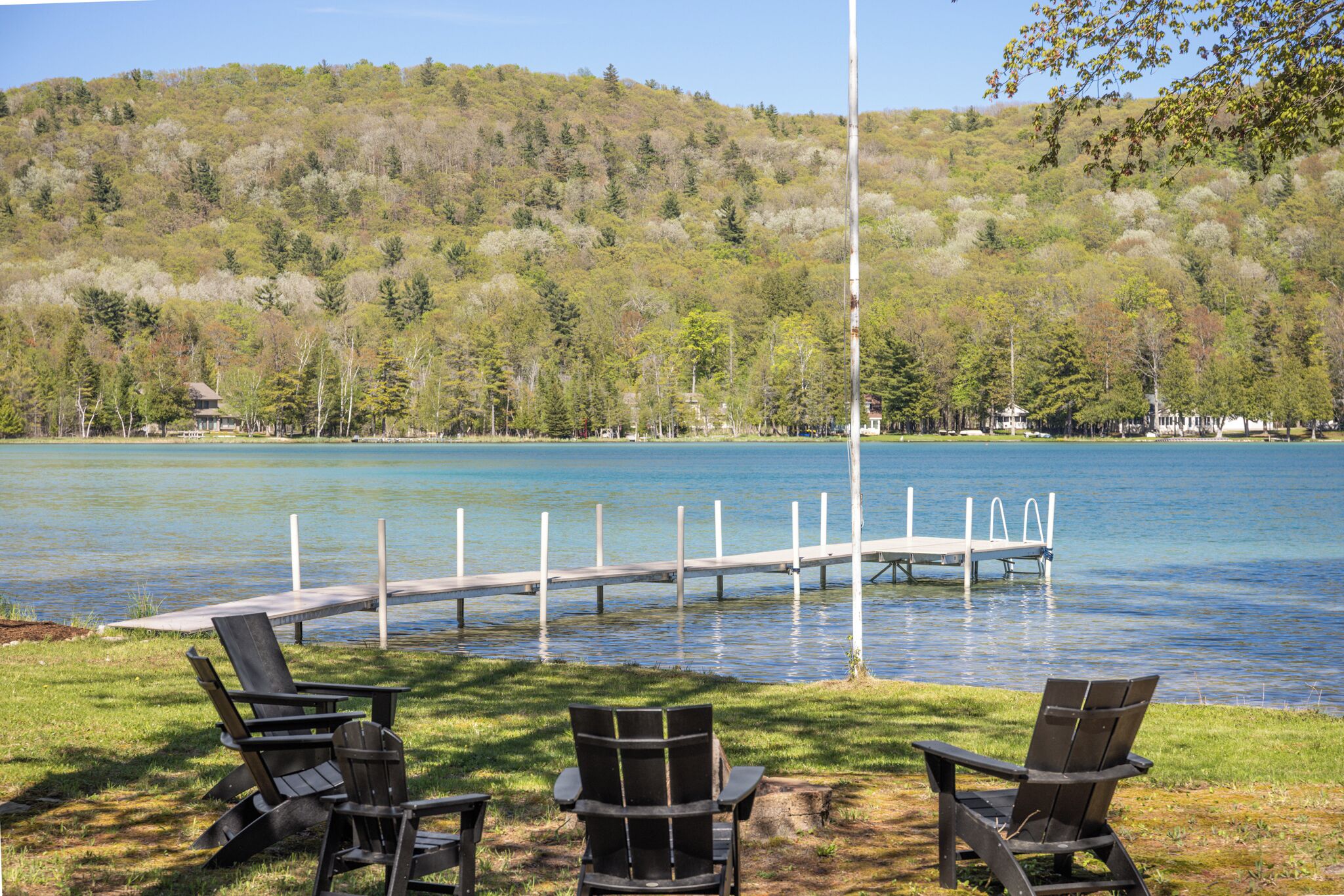 A lakeside view with dock, chairs, and a forested hill.