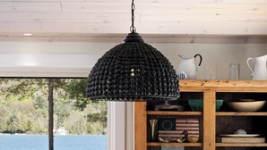 A dining area with a round table, four chairs, a black pendant light, and a view of the outdoors.