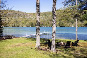 A lakeside view with trees, a dock, and chairs.