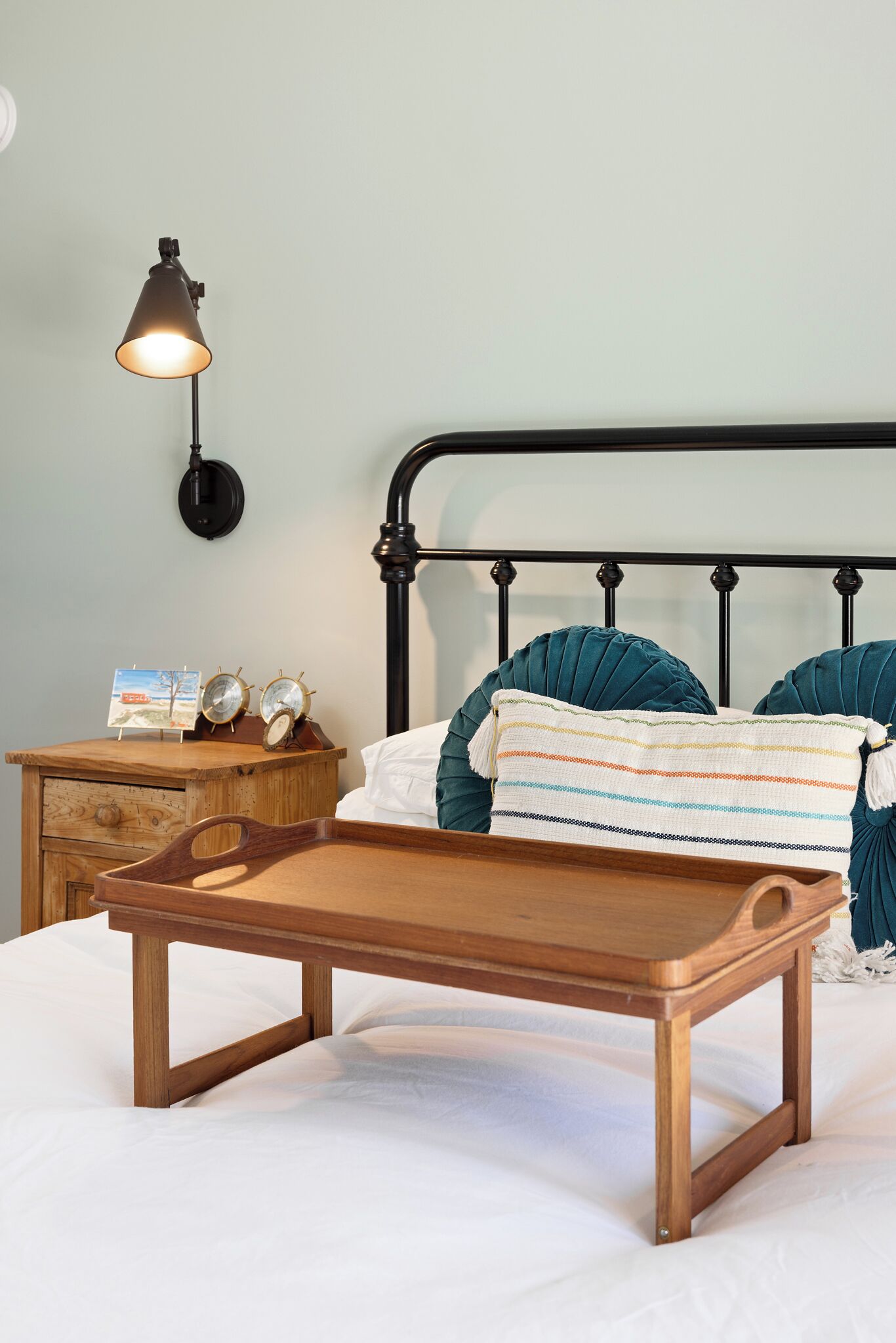 A bed with a wooden frame, a bedside table with a lamp, and two clocks.