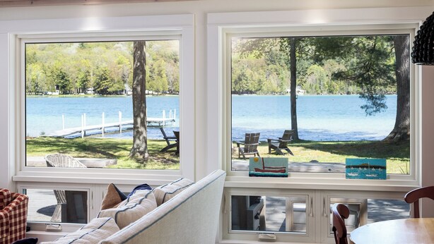 A room with a view of a lake, a sofa, and a table with chairs.