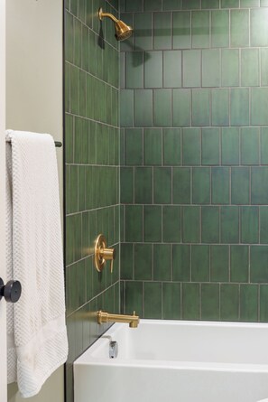 A bathroom with a white bathtub, green tiled walls, and a gold showerhead.