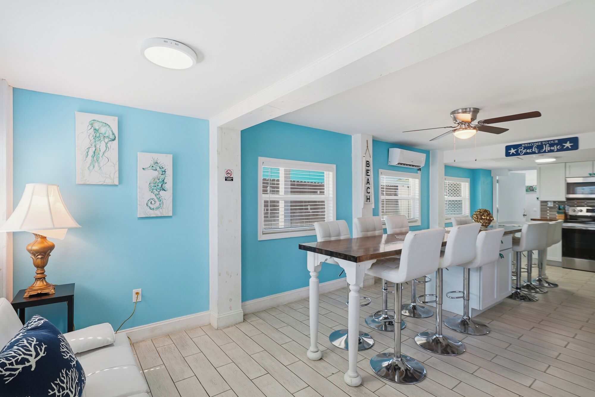 Een keuken met witte kastjes, een plafondventilator en een bordje met de tekst 'Welcome to our Beach House'.