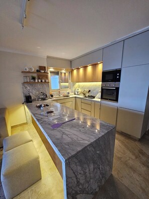 Cocina moderna con una isla de mármol, electrodomésticos integrados y una ventana.